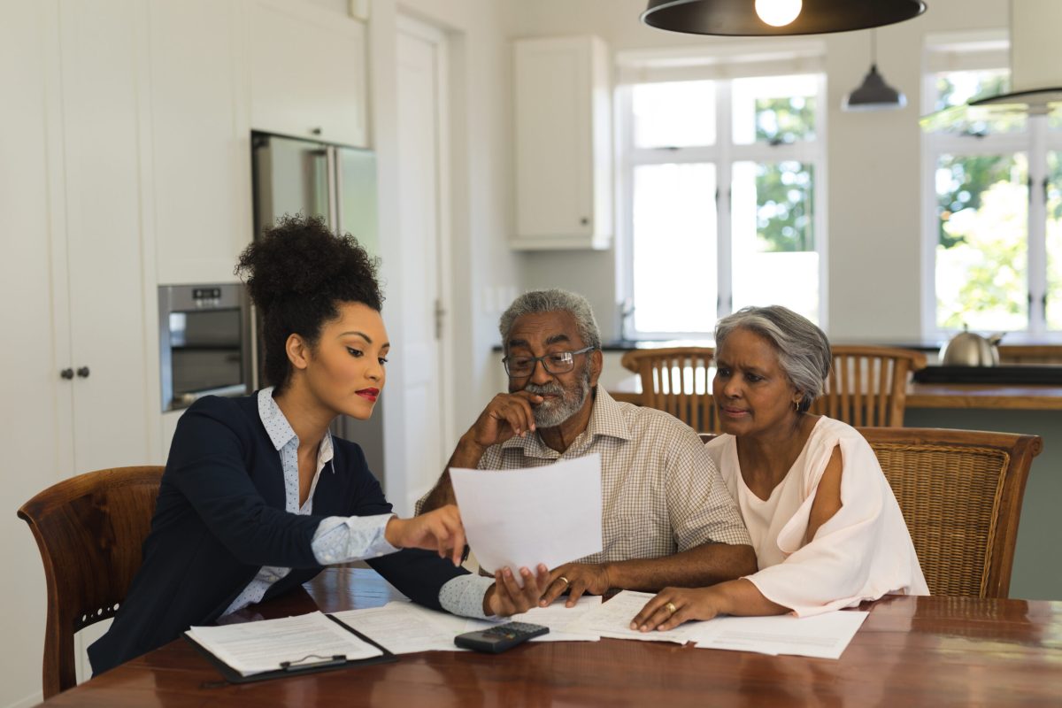 Front view of a female African American  real estate agent and senior couple discussing over documents at the table of the living room at home