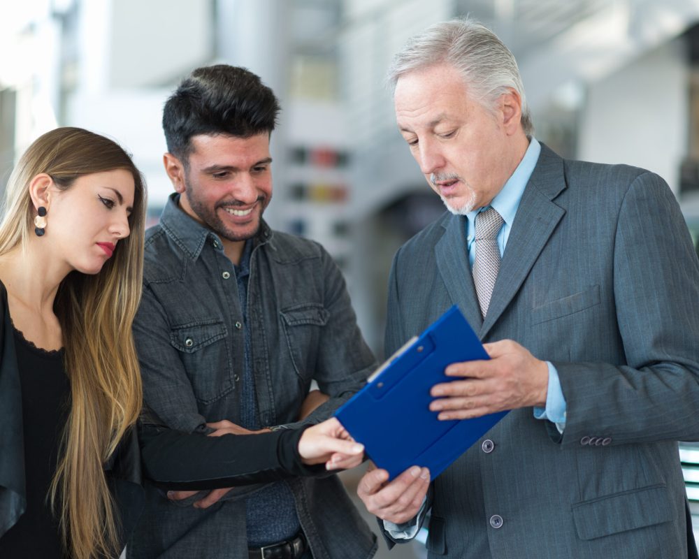 Happy young family talking to the salesman in a car showroom